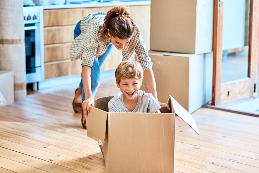 Mother pushing son around new home in moving box
